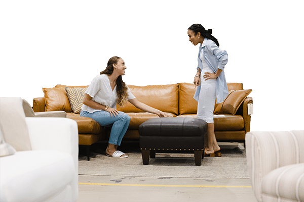 Two women testing a leather couch at Green Front Furniture.
